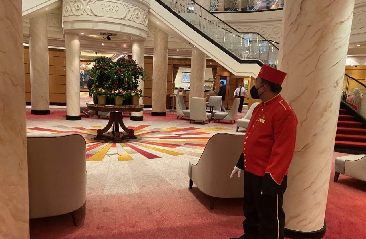 Cunard crew red uniform with hat and white gloves in the Queen Mary 2's atrium